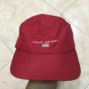 May include: Red baseball cap with a white embroidered logo that says "Ralph Lauren Polo Sport" and a small American flag.
