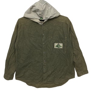 May include: A green long-sleeve button-up shirt with a gray hooded sweatshirt attached. The shirt has a patch pocket on the left chest with a logo that reads "SD Salt Water Design".