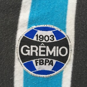 May include: A black and white circular patch with blue stitching. The patch features a football with the text "1903" above it, "GREMIO" in a large font, and "FBPA" below the football.