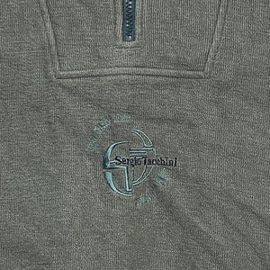 May include: A dark green sweater with a half-zip closure and a small embroidered logo that says "Sergio Tacchini".