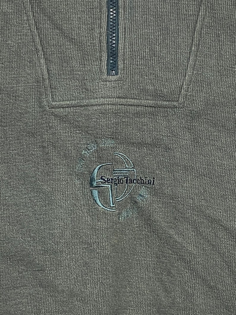 May include: A dark green sweater with a half-zip closure and a small embroidered logo that says "Sergio Tacchini".