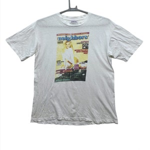 May include: White t-shirt with a graphic print of a magazine cover featuring a woman in a white top and the text "neighbors" in a red and black font.