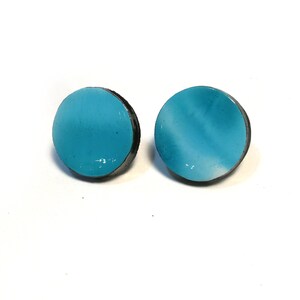 May include: A pair of blue and white enamel earrings with a black rim. The earrings are round and have a slightly textured surface.