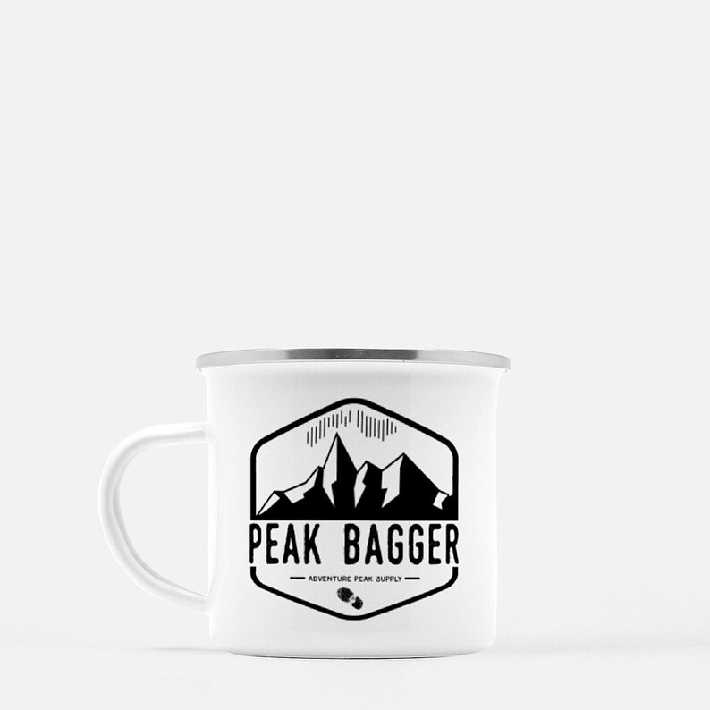 K&ouml;nnte beinhalten: Wei&szlig;e Emaille-Campingtasse mit einem schwarz-wei&szlig;en Logo, auf dem "Peak Bagger - Adventure Peak Supply" mit einer Bergkette abgebildet ist.