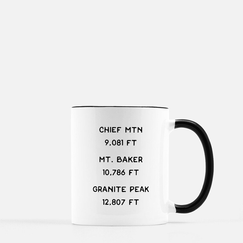 K&ouml;nnte beinhalten: Eine wei&szlig;e Keramiktasse mit schwarzem Rand und Henkel. Die Tasse hat schwarzen Text mit der Aufschrift "Chief Mtn 9,081 FT", "Mt. Baker 10,786 FT" und "Granite Peak 12,807 FT".