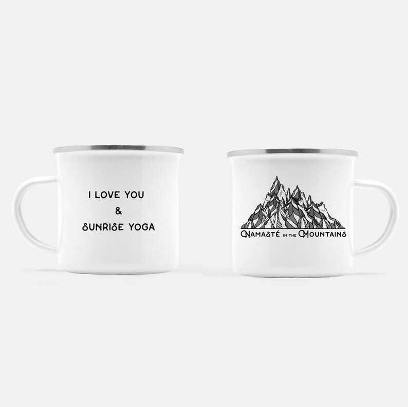 K&ouml;nnte beinhalten: Zwei wei&szlig;e Emaille-Tassen mit silbernen R&auml;ndern. Eine Tasse hat den Text "I LOVE YOU & SUNRISE YOGA" in Schwarz. Die andere Tasse zeigt eine Schwarz-Wei&szlig;-Bergillustration mit dem Text "NAMAST&Eacute; in the MOUNTAINS".