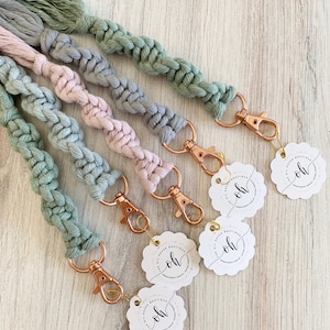 May include: Five keychains with braided rope strands in shades of green, gray, and pink. Each keychain has a gold-toned metal clasp and a circular tag with the text "Oh! Haven Boutique" in a cursive font.