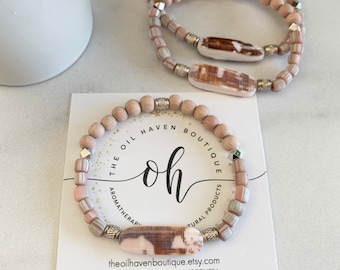 Può includere: Due braccialetti realizzati con perline di legno naturale e dettagli in conchiglia. I braccialetti sono impilati uno sopra l'altro e sono esposti su una carta bianca con il testo "The Oil Haven Boutique, Aromatherapy & Natural Products, theoilhavenboutique.etsy.com, Handmade in Appleton, Wisconsin".