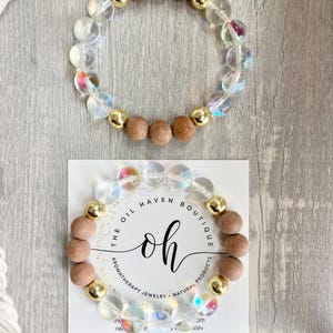 Peut inclure: Bracelet d'aromathérapie composé de perles transparentes, irisées et en bois, ainsi que de perles dorées. Le bracelet est présenté sur une carte avec le texte "THE OIL HAVEN BOUTIQUE".