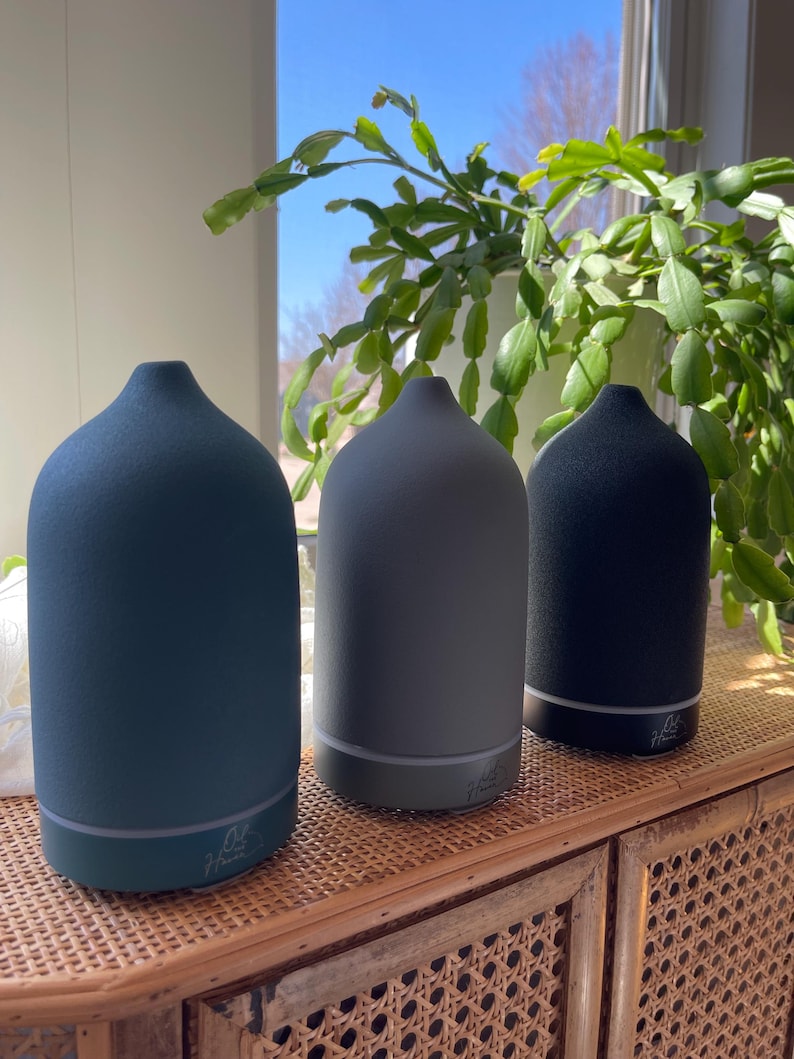 Puede incluir: Tres difusores de aceites esenciales en tonos azul, gris y negro se exhiben sobre un mueble tejido. Cada difusor tiene una parte superior redondeada y una base con una luz sutil. Los difusores est&aacute;n etiquetados con el texto "Haver".