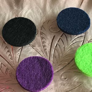 Peut inclure: Six diffuseurs ronds en feutre de diff&eacute;rentes couleurs, dont noir, bleu marine, violet, vert et rose. Les diffuseurs sont dispos&eacute;s sur une surface blanche textur&eacute;e.