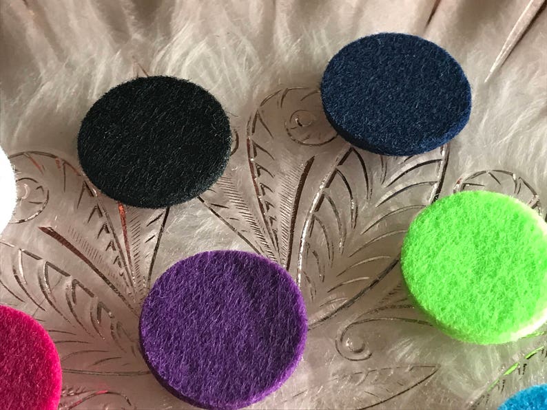 Peut inclure: Six diffuseurs ronds en feutre de diff&eacute;rentes couleurs, dont noir, bleu marine, violet, vert et rose. Les diffuseurs sont dispos&eacute;s sur une surface blanche textur&eacute;e.