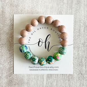 Peut inclure: Un bracelet en bois et silicone avec des motifs floraux verts. Le bracelet est sur une carte blanche avec le texte "The Oil Haven Boutique" et "oh" en écriture cursive. La carte comprend également le site Web "theoilhavenboutique.etsy.com" et le texte "Handmade in Appleton, Wisconsin".