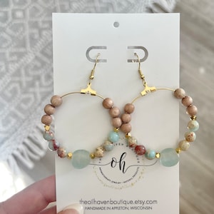 May include: Gold hoop earrings with light blue and brown beads. The earrings are displayed on a white card with the text "The Oil Haven Boutique" and "Handmade in Appleton, Wisconsin".