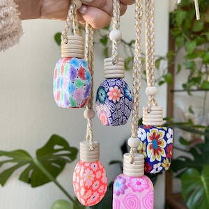 May include: Five small, decorative hanging glass bottles with patterned exteriors, each topped with a ribbed wooden cap and suspended by a braided cord with gold metallic threading and a small wooden bead accent.