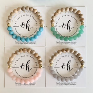 May include: Four bracelets with wooden beads and a second row of gemstone beads. The bracelets are displayed on white cards with the text "The Oil Haven Boutique" and "oh" in a handwritten font. The cards also include the text "aromatherapy jewelry natural products" and the website address "theoilhavenboutique.etsy.com".
