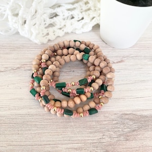 Pode incluir: Um conjunto de pulseiras de contas de madeira com detalhes verdes e rosados. As pulseiras estão empilhadas sobre uma superfície de madeira.