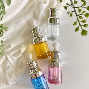 Puede incluir: Cuatro botellas de vidrio con gotero, con tapas plateadas y goteros blancos. Las botellas est&aacute;n llenas de l&iacute;quidos de diferentes colores: transparente, amarillo, rosa y azul.