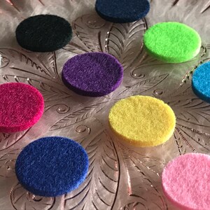 Peut inclure: Dix coussinets ronds en feutre de diff&eacute;rentes couleurs, dont rose, bleu, jaune, vert, violet, noir et blanc. Les coussinets sont dispos&eacute;s sur une surface d&eacute;corative.