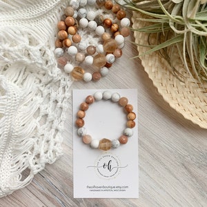 May include: A bracelet made with natural stones and wood beads. The bracelet is brown, white, and beige. The bracelet is on a white card with the text "The Ol' Haven Boutique" and "Handmade in Appleton, Wisconsin".