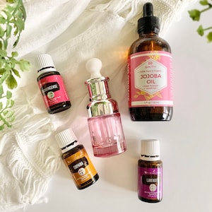 Puede incluir: Cinco botellas de aceite esencial con tapas y etiquetas blancas. Las botellas est&aacute;n sobre una superficie blanca con una tela de crochet blanca en el fondo. Las etiquetas dicen "Frankincense", "Copaiba", "Lavender" y "Jojoba Oil".