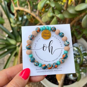 May include: A beaded bracelet featuring round, multi-colored turquoise and orange stone beads, light brown wooden beads, and small turquoise spacer beads. A circular gold-toned metal charm is attached, engraved with the text Eternal Happiness.