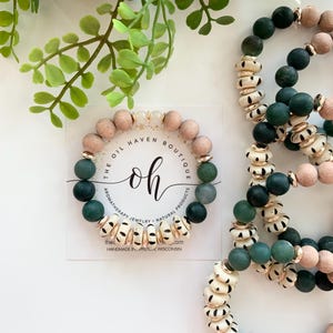 Op de afbeelding: Een set van drie armbanden met groene en witte kralen met gouden accenten. De armbanden zijn handgemaakt en bevatten de tekst "The Oil Haven Boutique" en "oh".