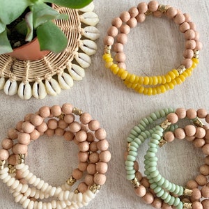 Puede incluir: Cuatro pulseras hechas de cuentas de madera y detalles dorados. Dos pulseras están hechas de cuentas de madera natural, una es verde y la otra es amarilla.