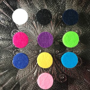 Peut inclure: Neuf cercles en feutre de diff&eacute;rentes couleurs, dont blanc, noir, bleu marine, rose, violet, vert, jaune et bleu clair. Les cercles sont dispos&eacute;s en cercle sur un fond argent&eacute;.