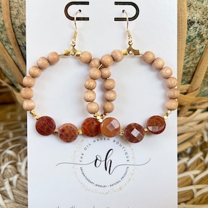 Op de afbeelding: Een paar houten hoepeloorringen met bruine agaat kralen en gouden accenten. De oorringen worden getoond op een witte kaart met de tekst "THE OIL HAVEN BOUTIQUE oh AROMATHERAPY JEWELRY NATURAL PRODUCTS theoilhavenboutique.etsy.com HANDMADE IN APPLETON, WISCONSIN".