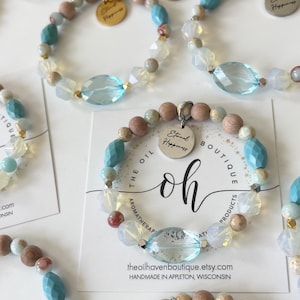 May include: Several aromatherapy bracelets with a mix of light blue, clear, and wooden beads. Each bracelet features a large, faceted light blue bead and a small metal charm that says "Eternal Happiness". The bracelets are displayed on white cards.