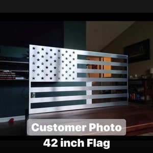 May include: A silver metal American flag wall decor with a 42 inch size. The flag is mounted on a wooden surface.