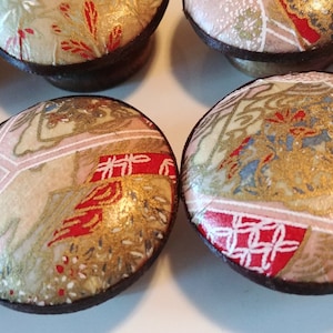 May include: A collection of decorative cabinet knobs with a Japanese-inspired design. The knobs feature a mix of beige, pink, and red patterned fabric with gold accents, set on dark brown bases. The knobs are arranged on a white surface.