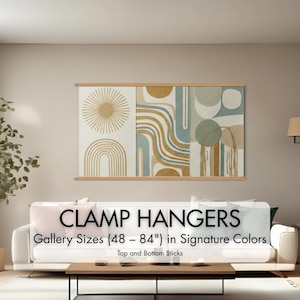 May include: A large, abstract art piece with a sunburst, arches, and geometric shapes in gold, blue, and green tones, displayed with wooden clamp hangers. The text reads "CLAMP HANGERS Gallery Sizes (48 - 84") in Signature Colors".