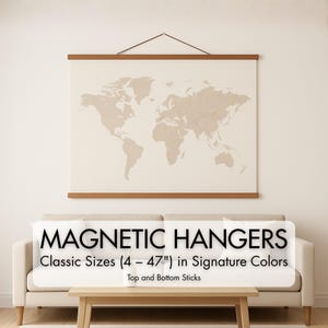 Op de afbeelding: Een wereldkaart in beige tinten, gepresenteerd met magnetische hangers. De kaart is gemonteerd op een lichtgekleurde achtergrond, met houten boven- en onderstokken. De tekst "MAGNETIC HANGERS Klassieke maten (10 - 119 cm) in Signature Colors Top and Bottom Sticks" staat eronder.