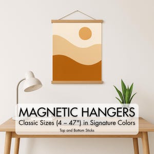 May include: A framed abstract art print with a minimalist design. The artwork features a sun and layered, wavy shapes in shades of beige, tan, and brown. The print is held by wooden magnetic hangers. The text on the image reads "MAGNETIC HANGERS" and "Classic Sizes (4 - 47") in Signature Colors".