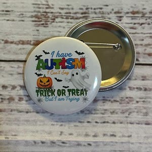 May include: A round button with the text "I have AUTISM I Can't Say TRICK OR TREAT But I am Trying" and Halloween-themed graphics. The button has a white background with a silver pin back. Another button is visible in the background.