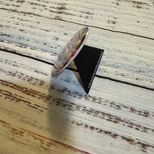 May include: A round, white button with a colorful, abstract design. The button is on a black stand.