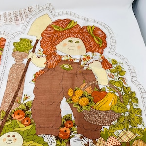 May include: A vintage fabric applique pattern featuring a red-haired girl with a basket of vegetables and a frog on a stone pedestal. The pattern is on a white background with green, brown, and yellow accents. The text "Leave Open for Stuffing" is printed at the bottom of the pattern.