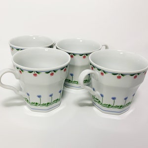 May include: Set of four white ceramic teacups with a floral design. The cups have a hexagonal shape and a small handle. The floral design features red and blue flowers with green leaves.