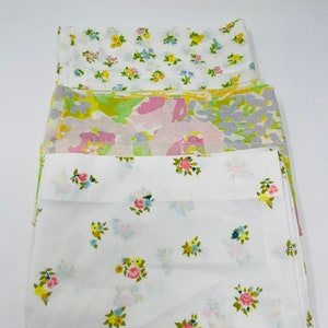 May include: Three fabric squares with floral patterns. The top square has a white background with small pink, yellow, and blue flowers. The middle square has a light green, pink, and gray abstract pattern. The bottom square has a white background with small pink, yellow, and blue flowers.