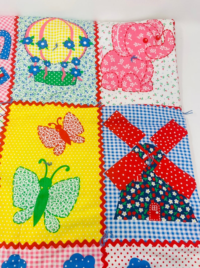 May include: A colorful patchwork quilt with a hot air balloon, elephant, butterfly, and windmill design. The quilt is made of different fabrics with various patterns, including gingham, polka dots, and floral prints.