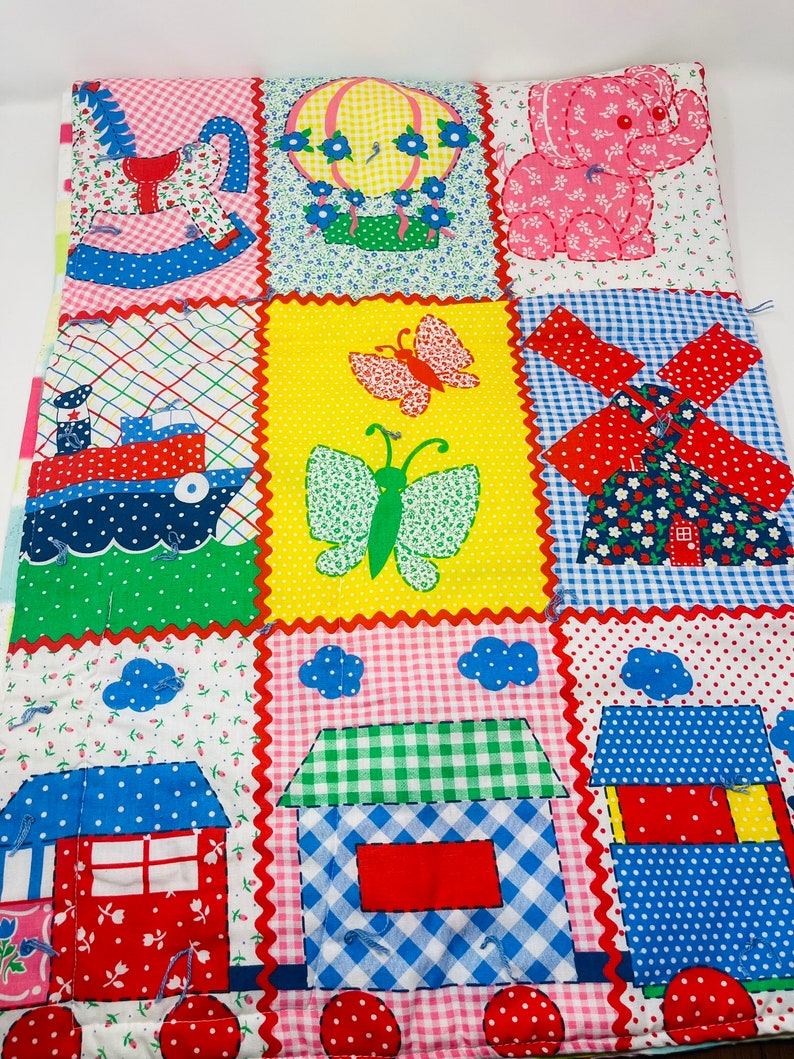 May include: A colorful patchwork quilt with various designs, including a rocking horse, hot air balloon, butterfly, windmill, and houses. The quilt is made of different fabrics and patterns, including gingham, polka dots, and floral prints.