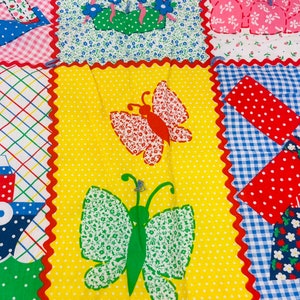 May include: A yellow fabric with a red, white, and blue checkered pattern. The fabric has a scalloped edge and is decorated with two butterflies, one green and one red. The butterflies are made of fabric with a floral pattern.