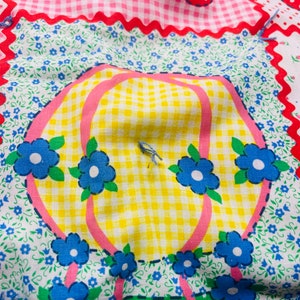May include: A patchwork fabric with a yellow and white gingham pattern, pink and blue flowers, and a pink and white polka dot pattern. The fabric has a whimsical design with a hot air balloon and a green and white polka dot pattern.