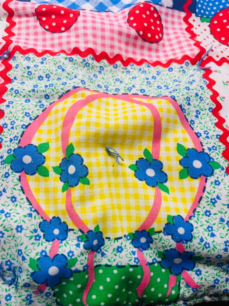 May include: A patchwork fabric with a yellow and white gingham pattern, pink and blue flowers, and a pink and white polka dot pattern. The fabric has a whimsical design with a hot air balloon and a green and white polka dot pattern.