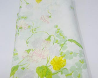 May include: A folded white fabric featuring a botanical print with light green eucalyptus-style leaves, delicate pink flowers, and bright yellow blossoms. The pattern includes thin green vines and stems connecting the floral elements across the surface.