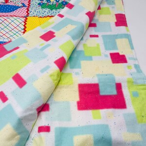 May include: A white blanket with a geometric pattern of pink, blue, and green squares. The blanket is folded in half and the pattern is visible on both sides.