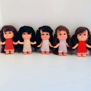 May include: Five small plastic dolls with black hair and pigtails wearing colorful dresses. The dolls have painted blue eyes and pink cheeks.