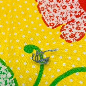 May include: A close-up of a blue and gray string on a yellow fabric with white polka dots and a red and white floral pattern.